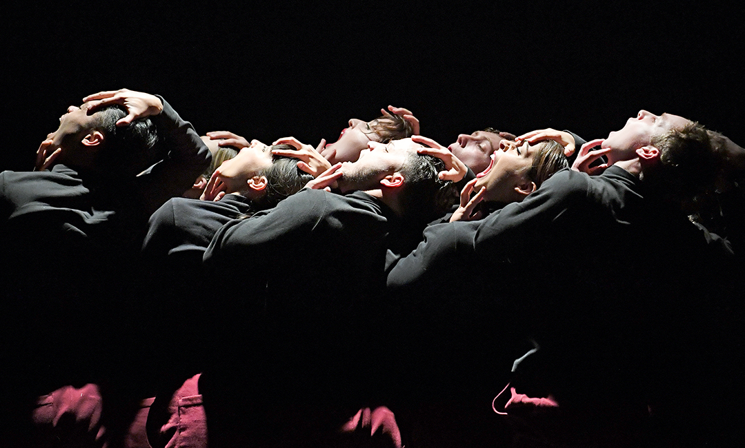 Group of dancers dressed in black on stage with dramatic lighting