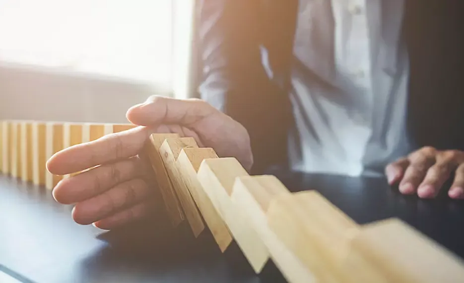 Businessman's hand blocking wooden blocks from falling over